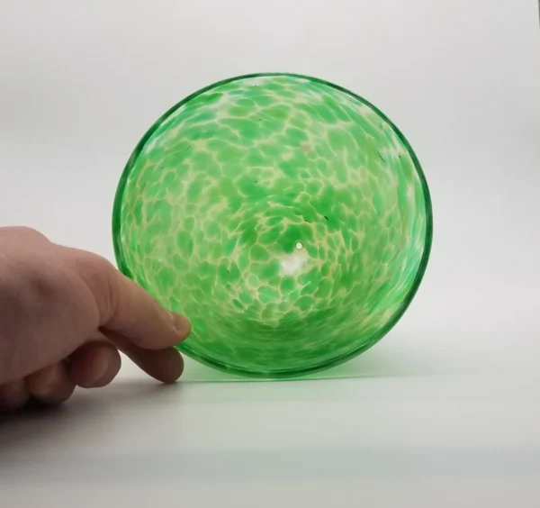 A person touching the bottom of a green glass bowl.