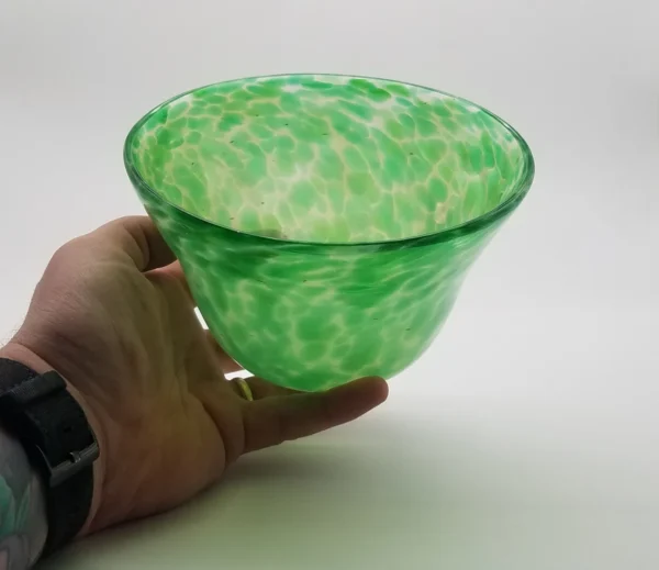 A hand holding a green bowl with white speckles.
