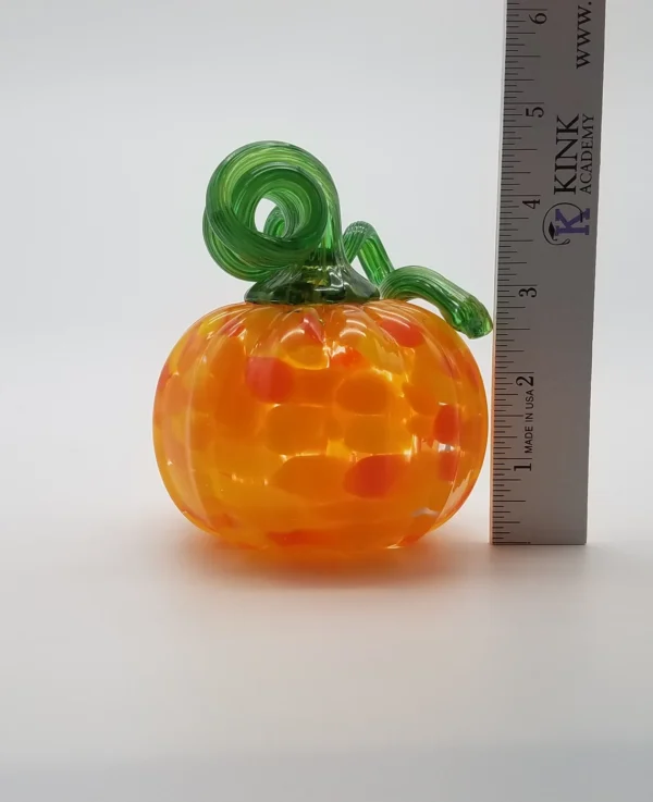 A glass pumpkin with a green stem on top of it.