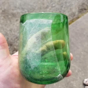 A person holding a green glass with a lime in it.