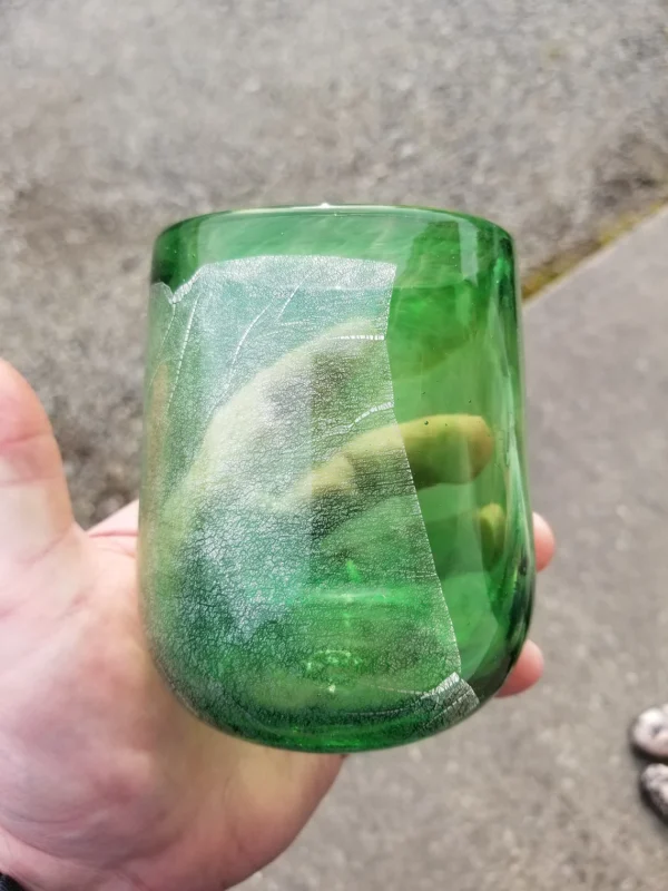 A person holding a green glass with a lime in it.