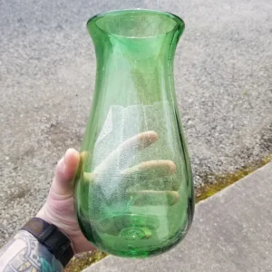 A person holding a green vase on the street.
