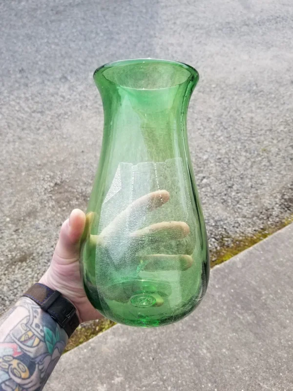 A person holding a green vase on the street.