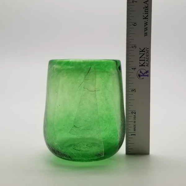 A green glass cup next to a measuring tape.