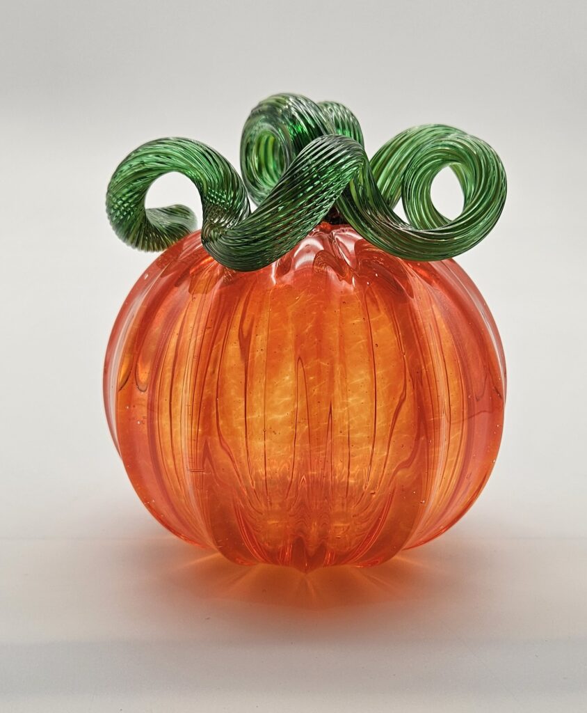 A glass pumpkin with green stems on top of it.