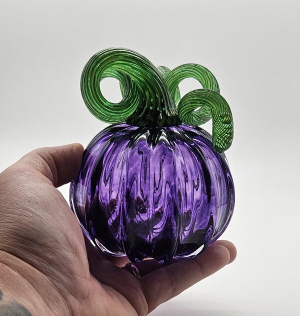 A person holding a purple glass pumpkin with green stems.